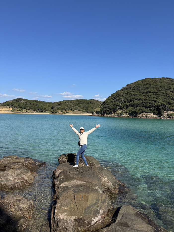 海の上にある岩の上に立ち手を広げてポーズをとる会長さんのお写真